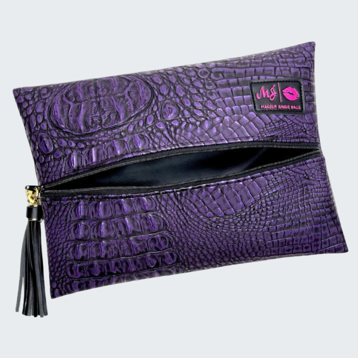 Purple crocodile-textured clutch bag with a tassel on a white background