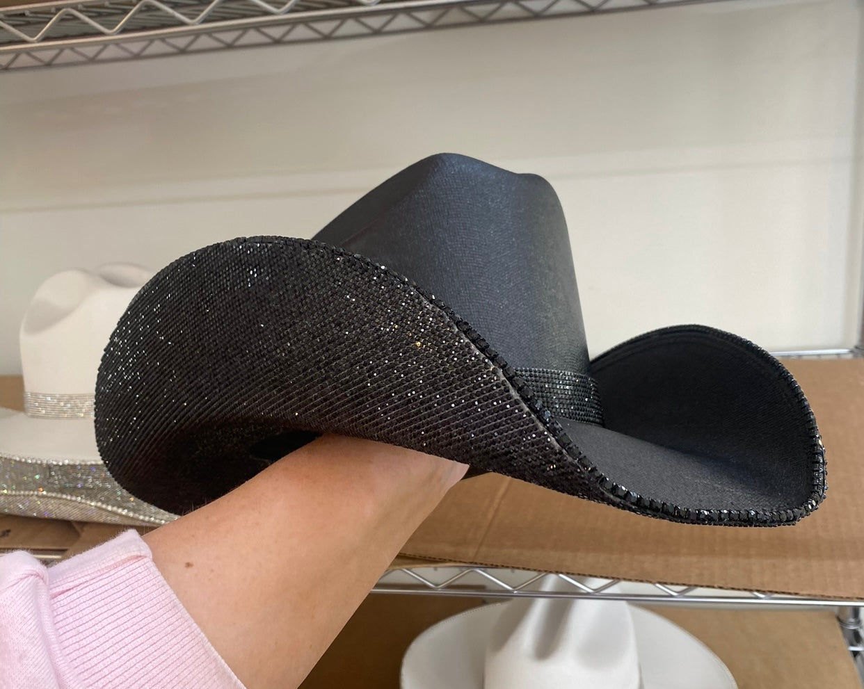 Black wide-brimmed hat held by a person with a neutral background