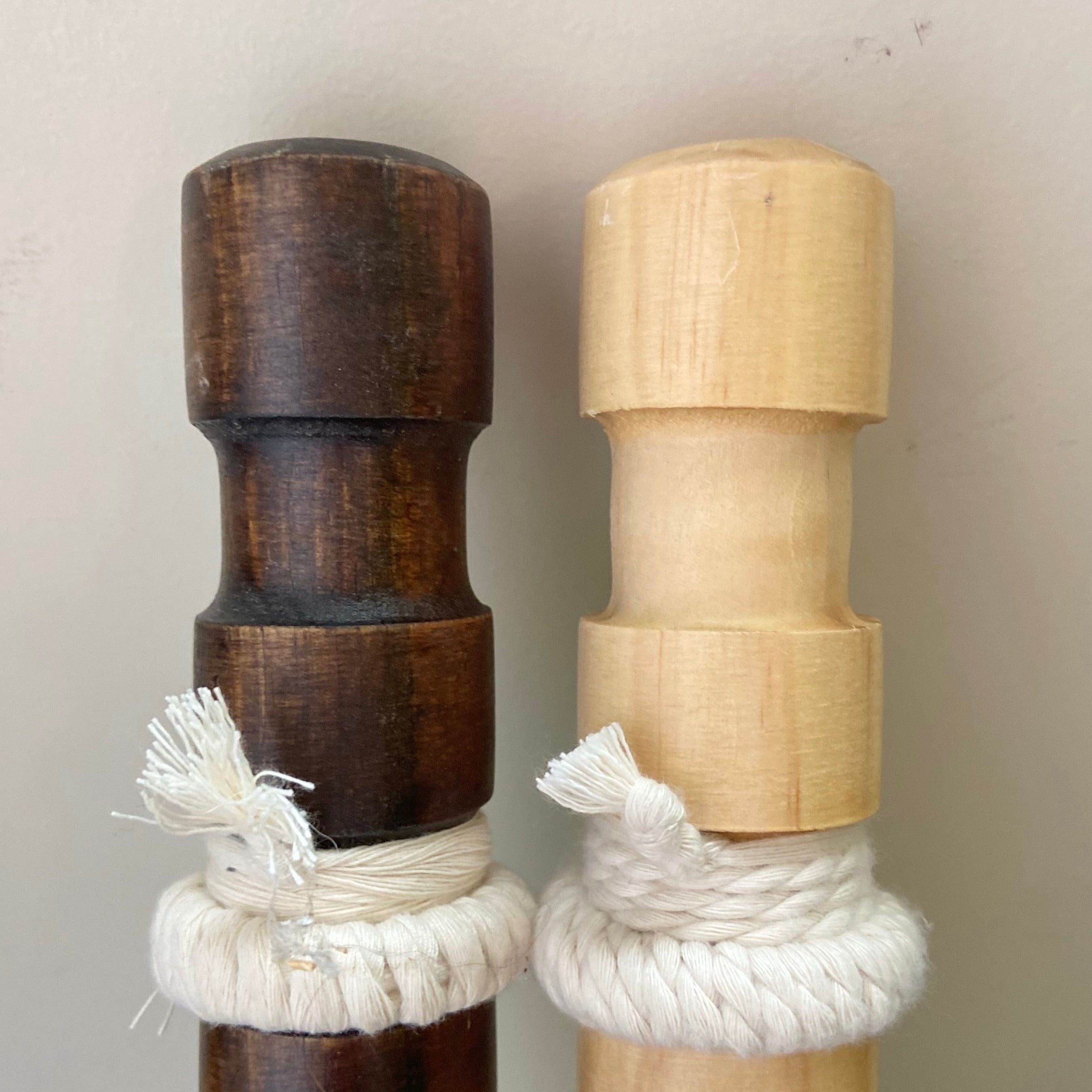 Two wooden pegs with rope ends, one dark brown and one light brown, on a neutral background.