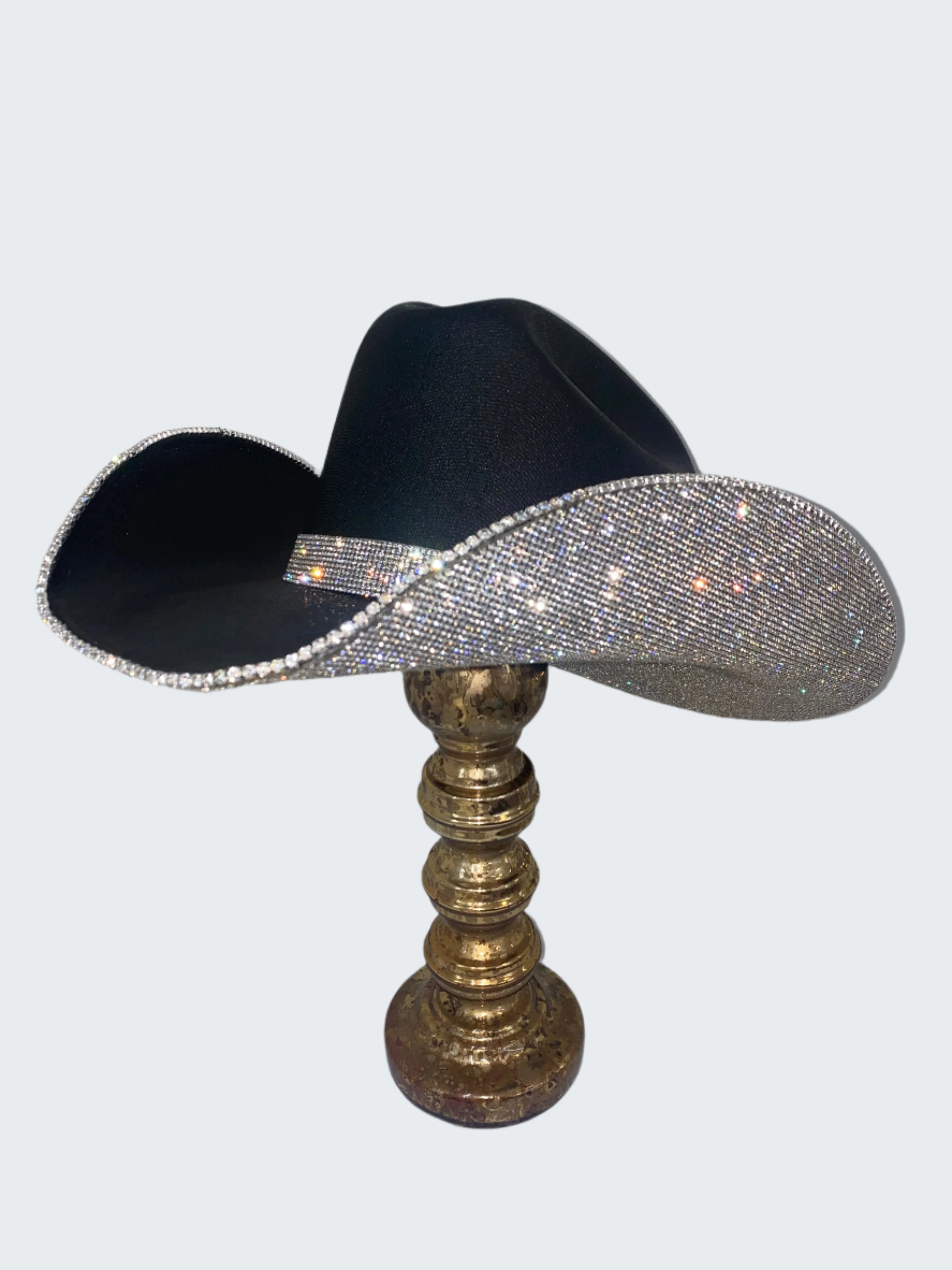 Black cowboy hat with silver bling on a decorative stand against a white background