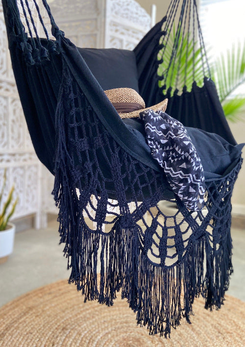 Black macrame hammock with fringe details, placed indoors.