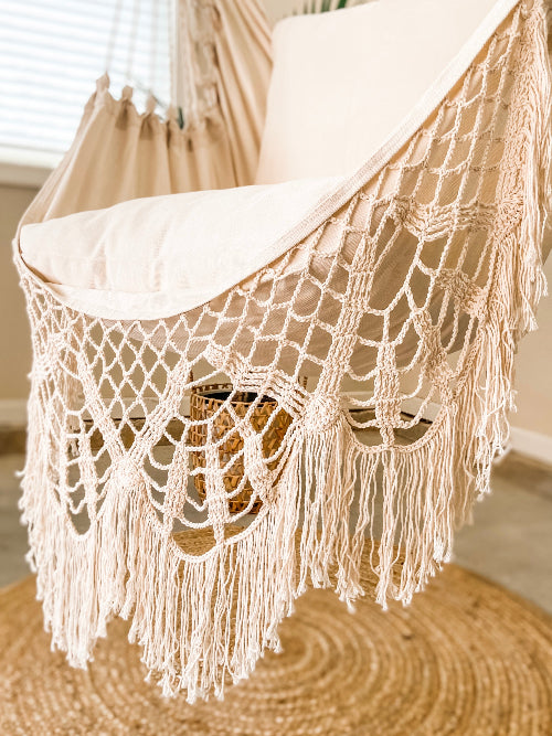 Macrame plant hanger with white cushions on a wooden surface