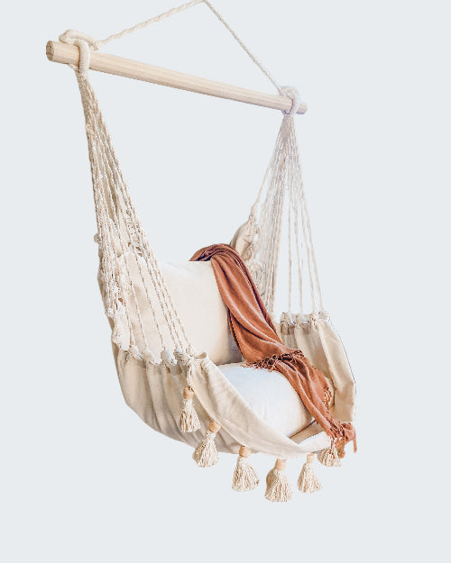 Macrame hanging chair with tassels in a cozy room with a plant and round rug.