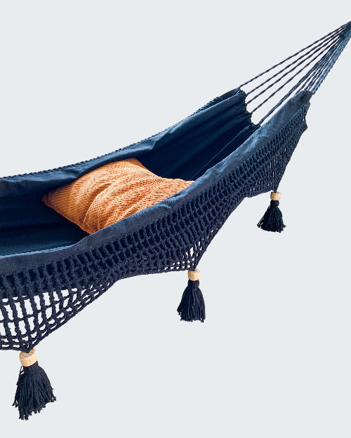 Navy blue hammock with orange pillow in a room with a plant and window.