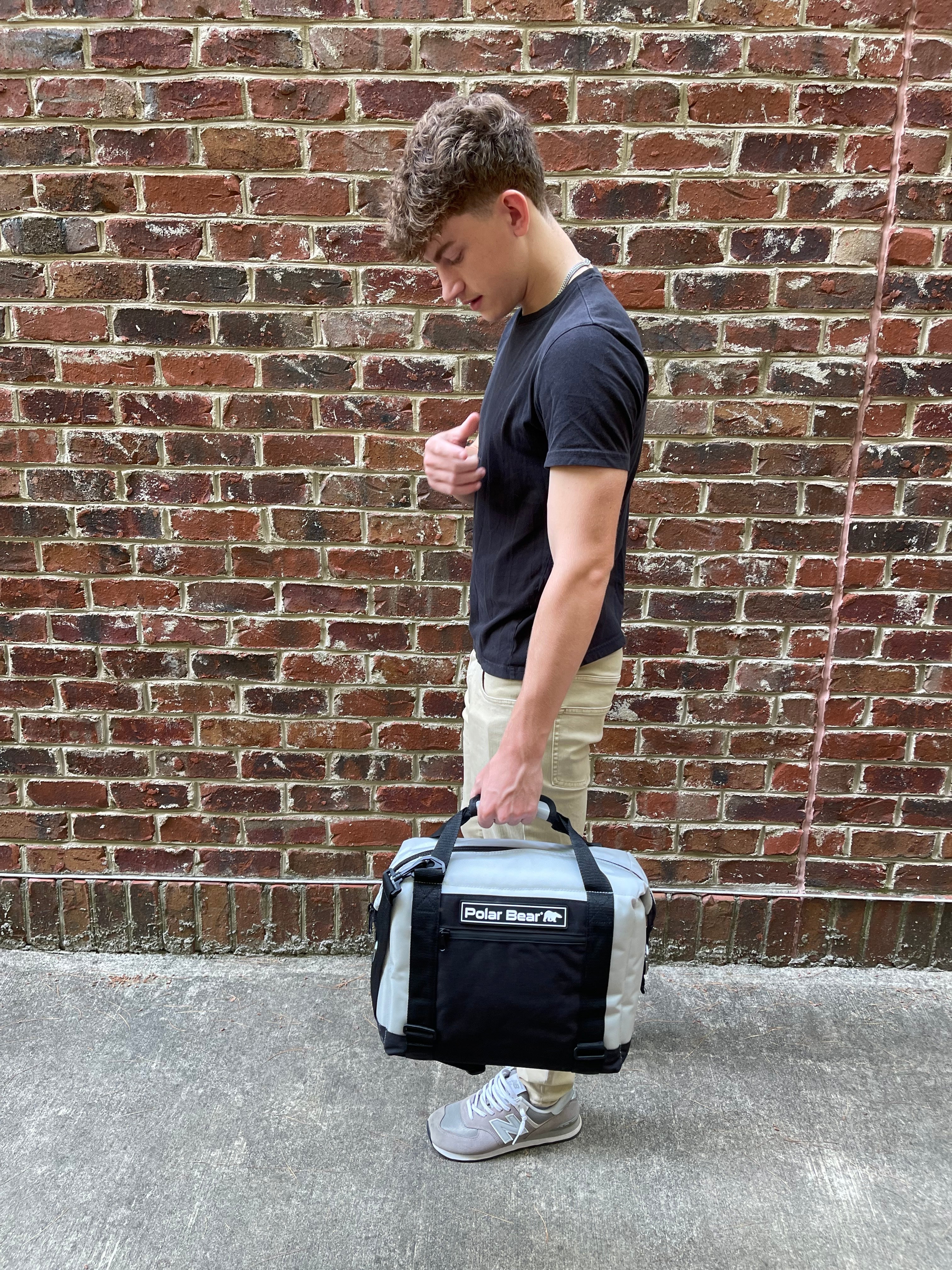 Person holding a black and gray duffel bag against a brick wall.