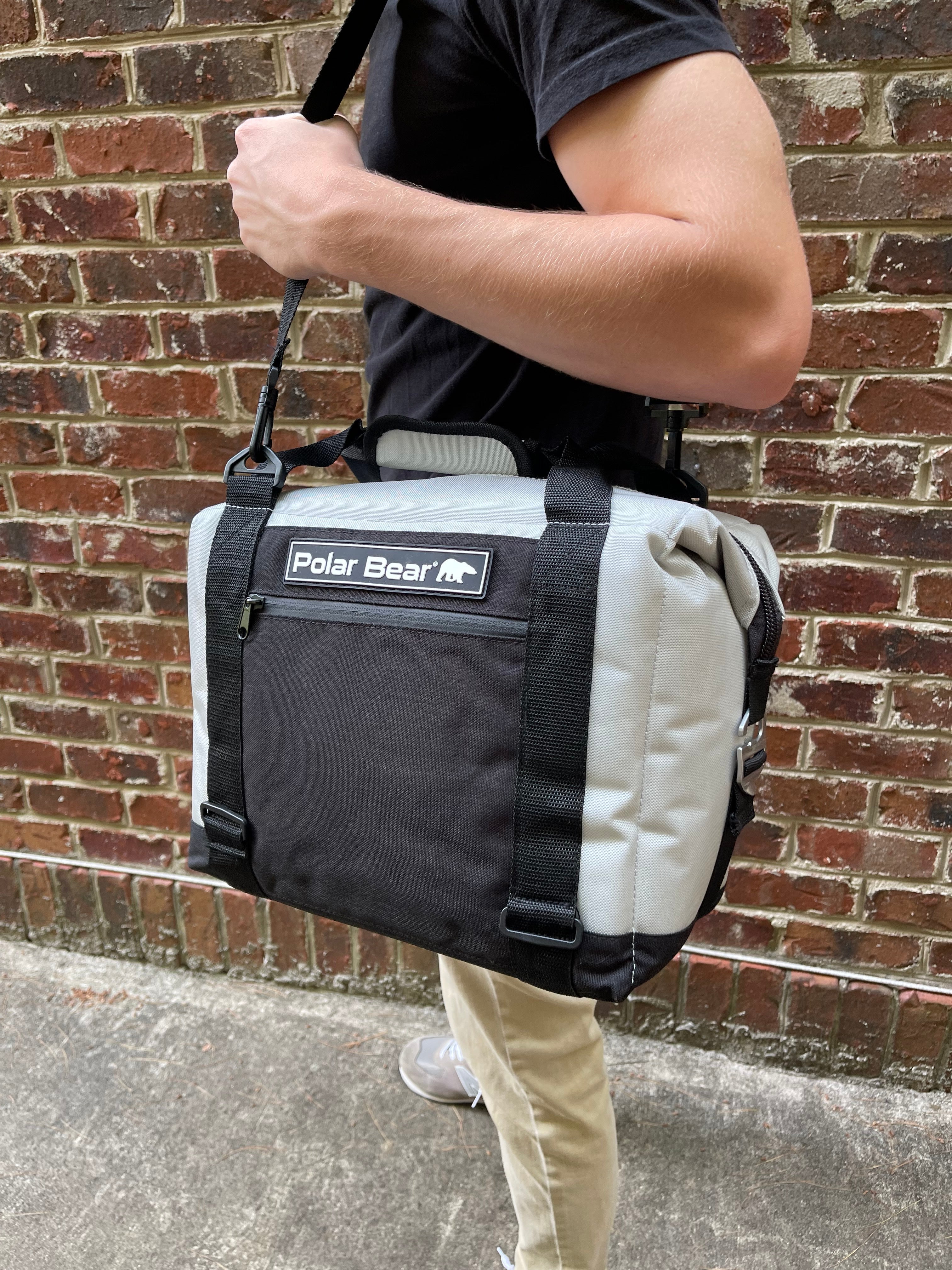 Person carrying a black and gray cooler bag with 'Polar Bear' logo against a brick wall.
