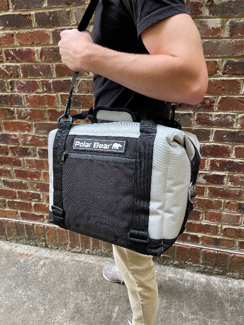 Person carrying a black and gray cooler bag with 'Polar Bear' logo against a brick wall.