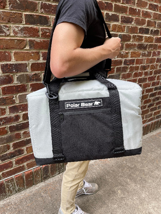 Person carrying a large insulated cooler bag with 'Polar Bear' branding against a brick wall.
