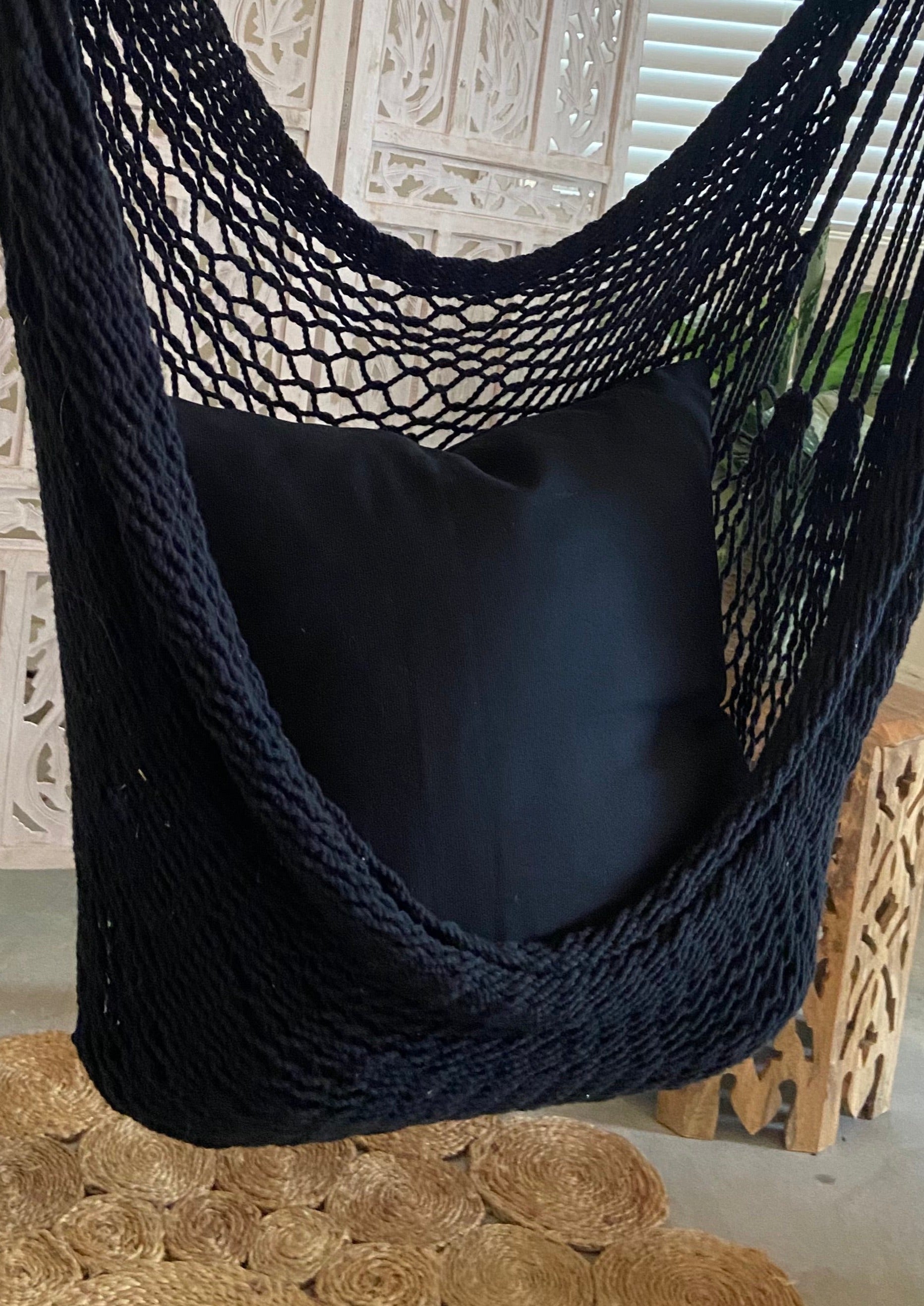 Black hammock chair with a pillow on a wooden floor.