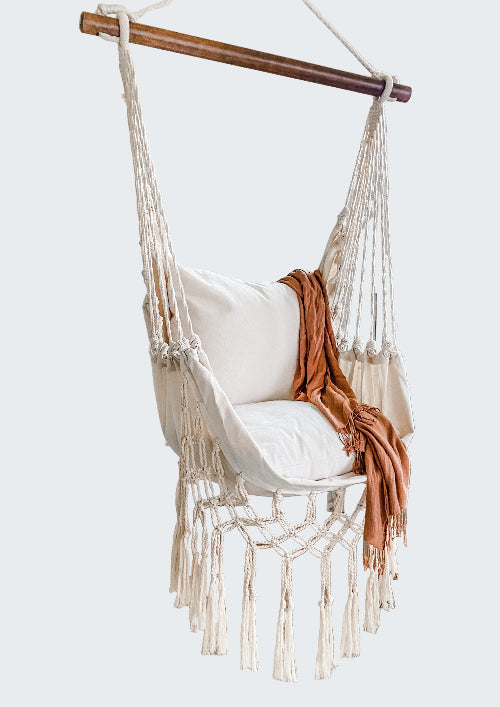 Macrame hammock chair with white cushion and brown blanket in a room with a white screen partition and plants.