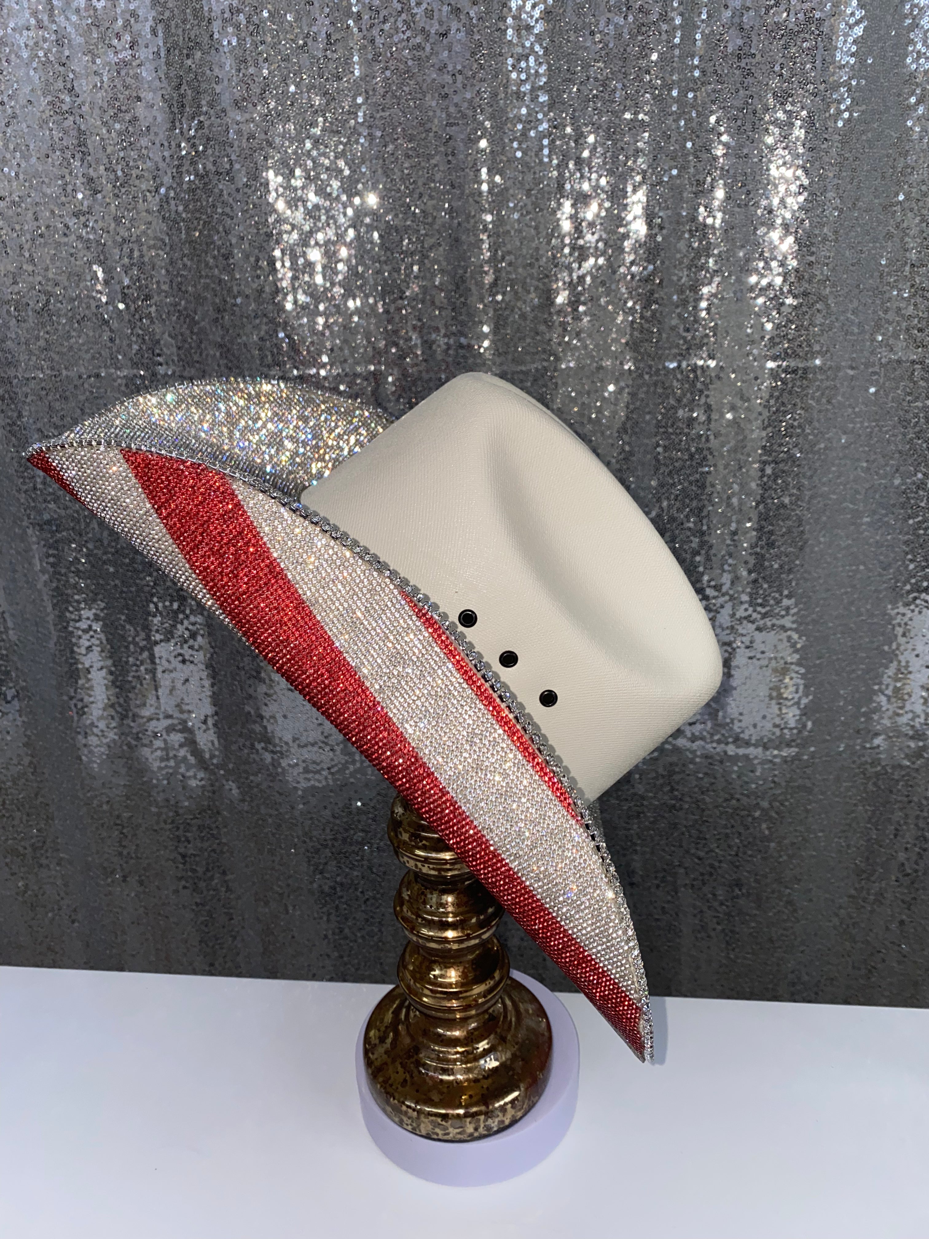 Decorative hat with red and gray striped band on a stand against a glittery silver background