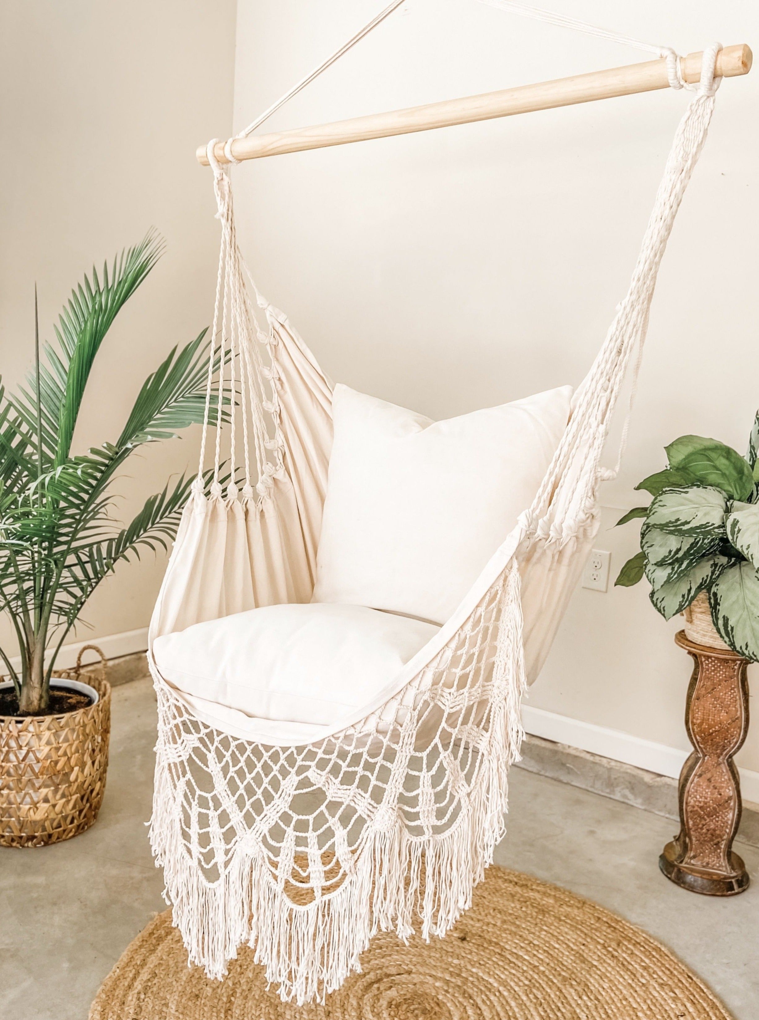 Macrame hammock chair with white cushion in a room with plants and a rug.