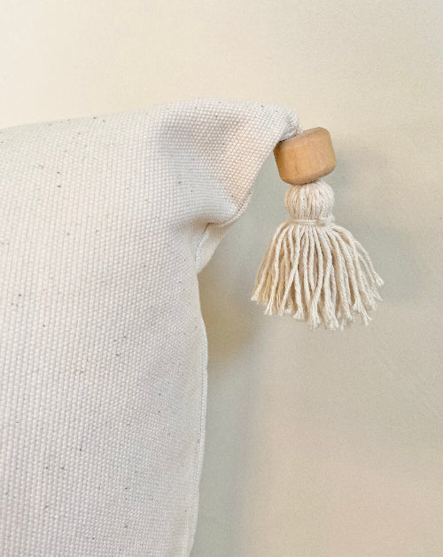 White pillow with a wooden ring and tassel on a neutral background
