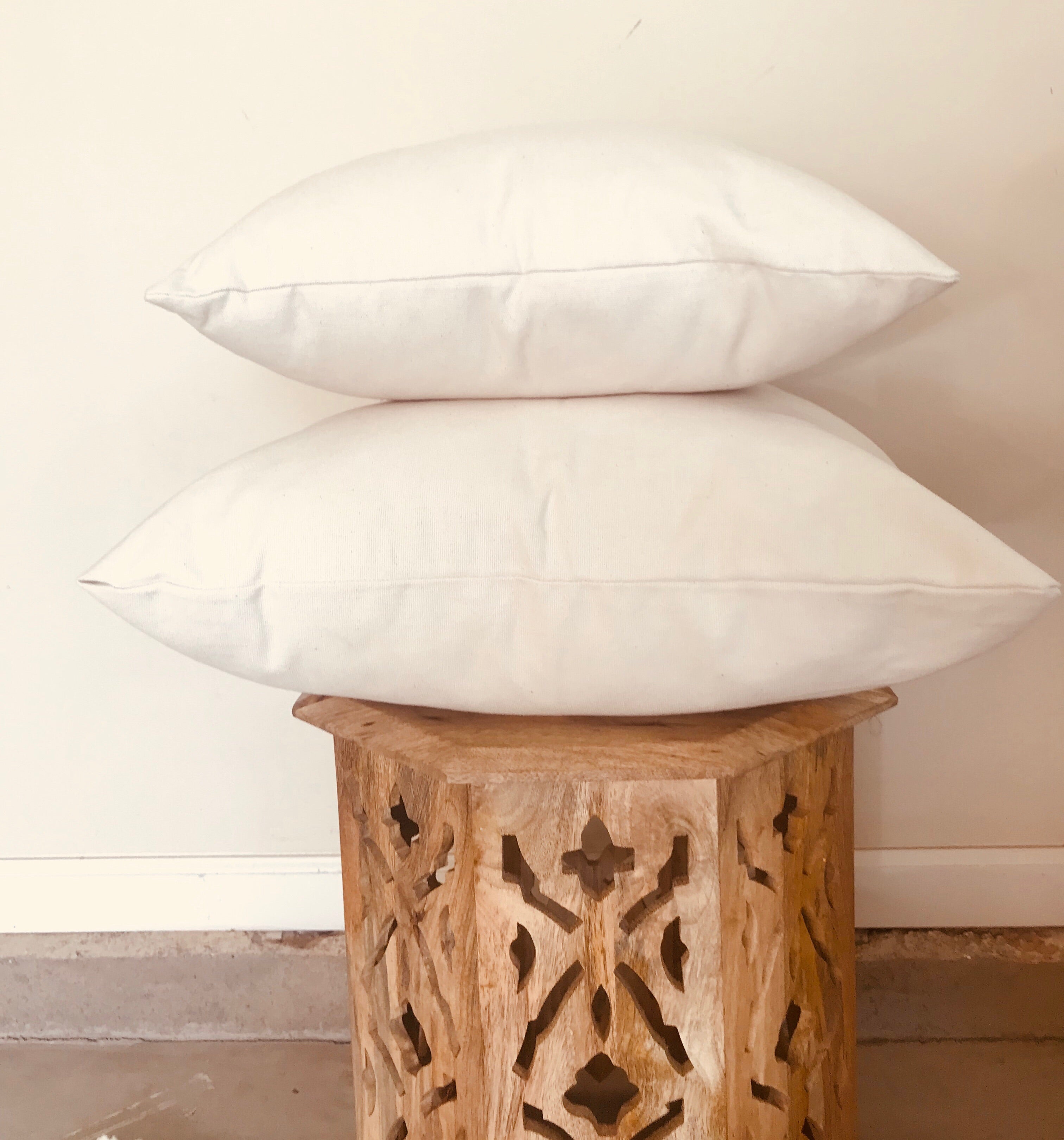 Two white pillows stacked on a wooden stool with a neutral background
