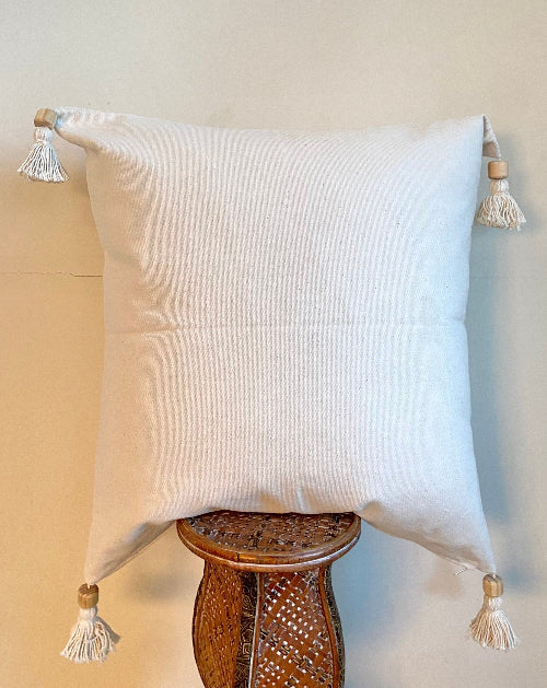 White pillow with tassels on a wooden stool against a beige wall