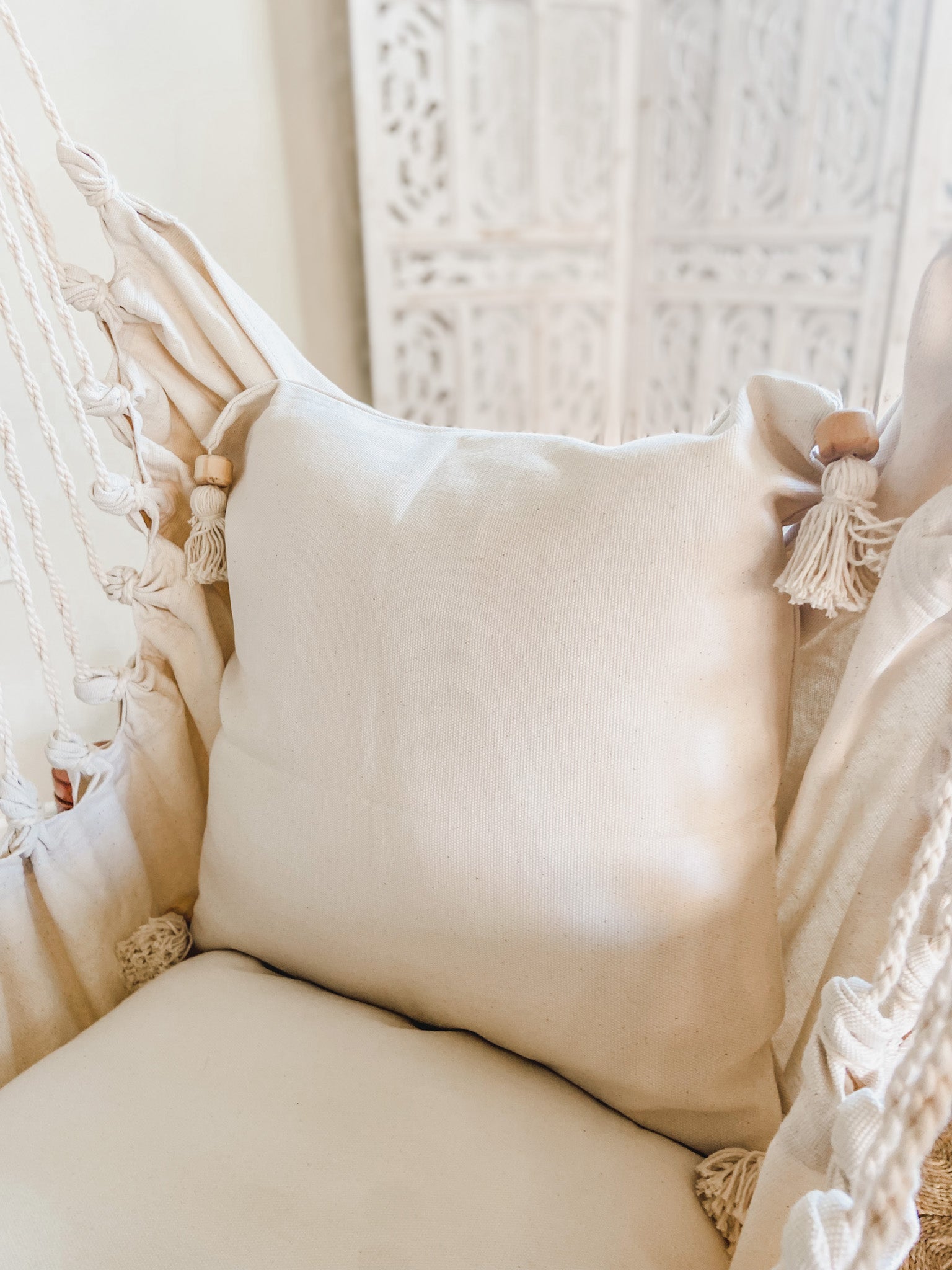 Cream-colored pillow with tassels on a textured chair