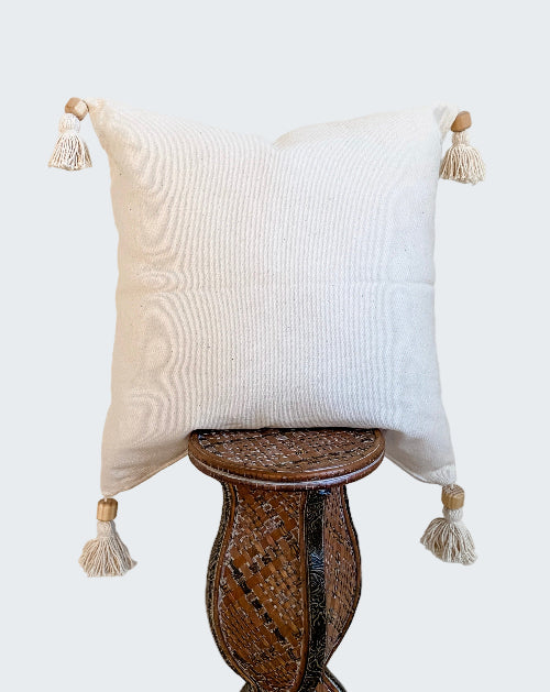 Decorative pillow with tassels on a wooden stool against a beige wall
