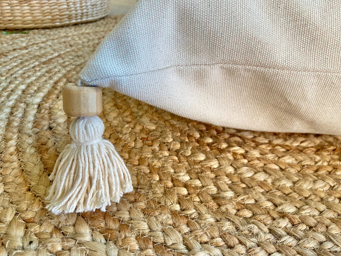 Beige fabric pillow with a tassel on a woven surface