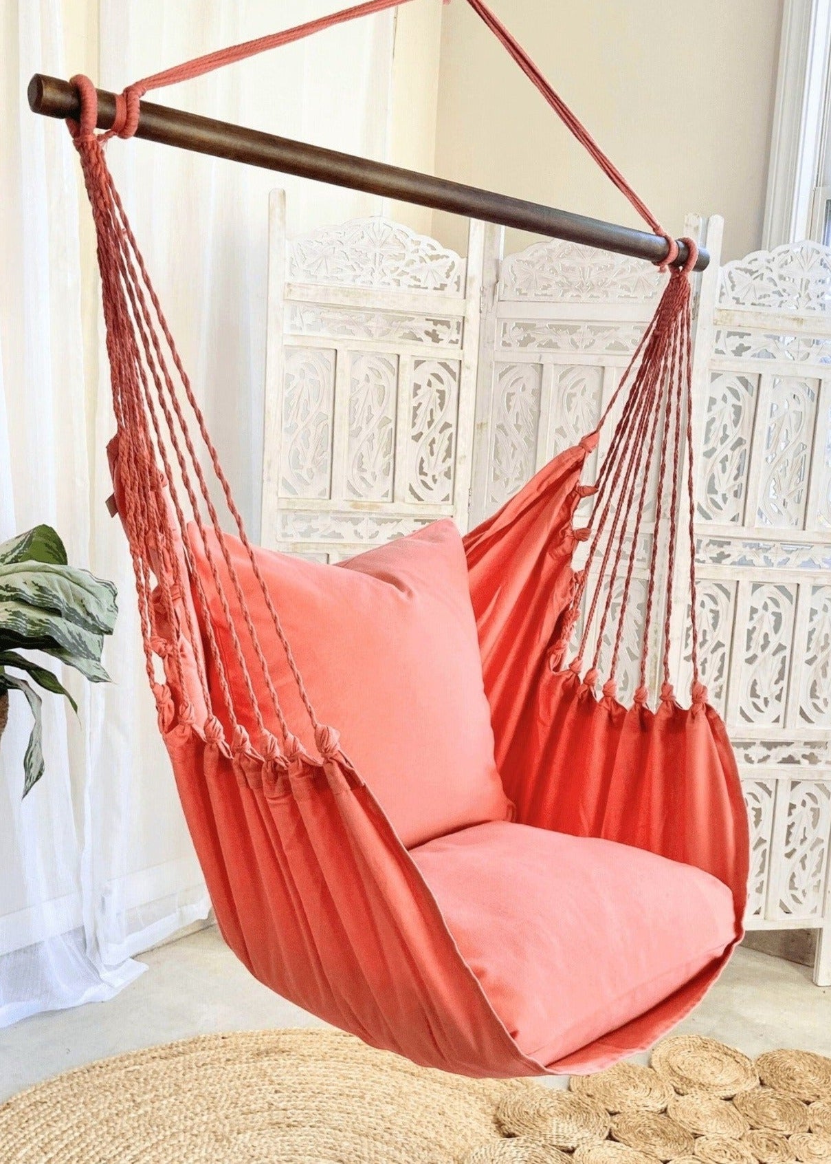 Coral hammock chair with pink cushions in a room with decorative elements.