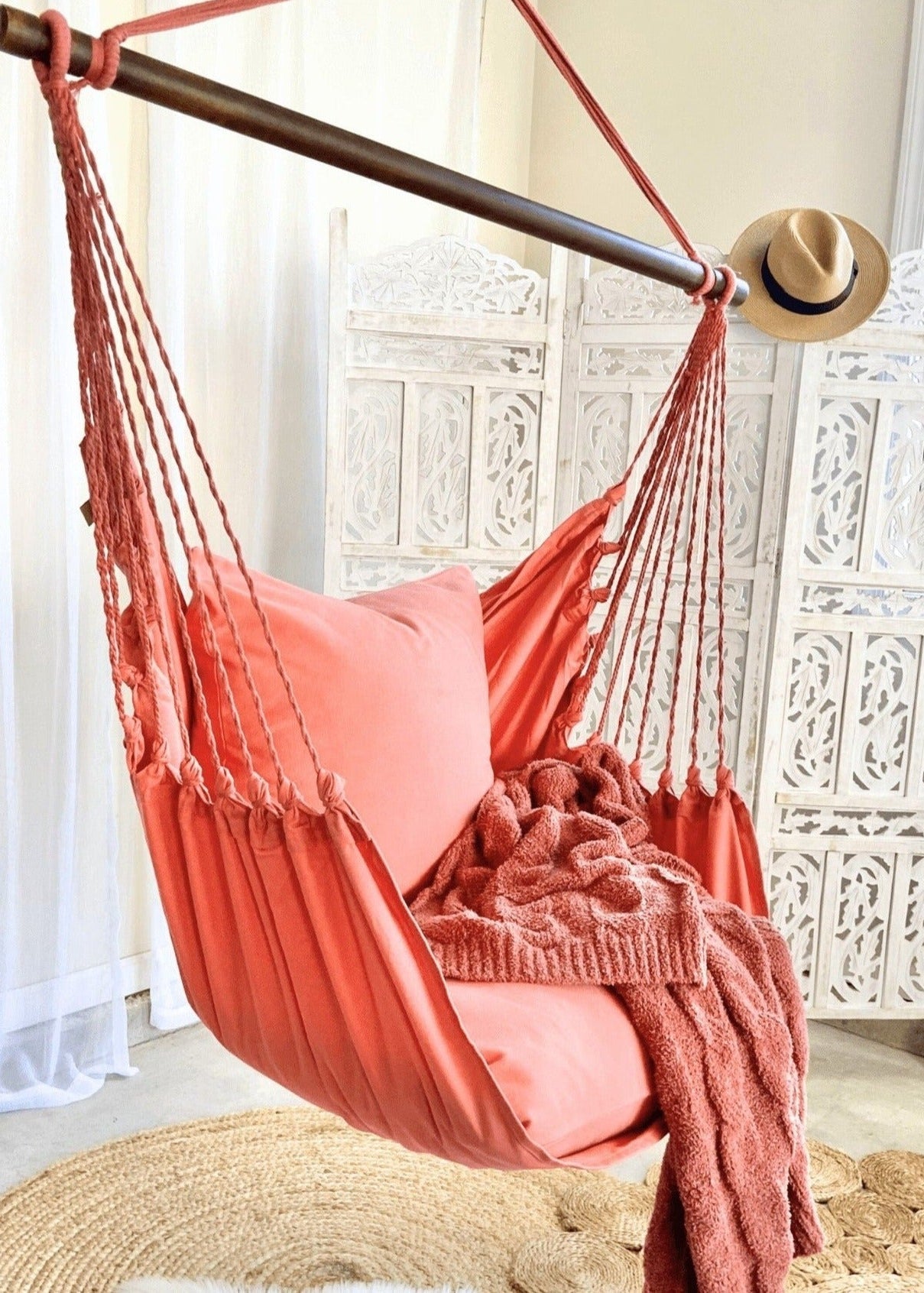 Coral hammock chair with pink cushions and a straw hat in a decorative room.