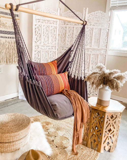 Brown hammock chair with colorful pillows in a cozy room setting.