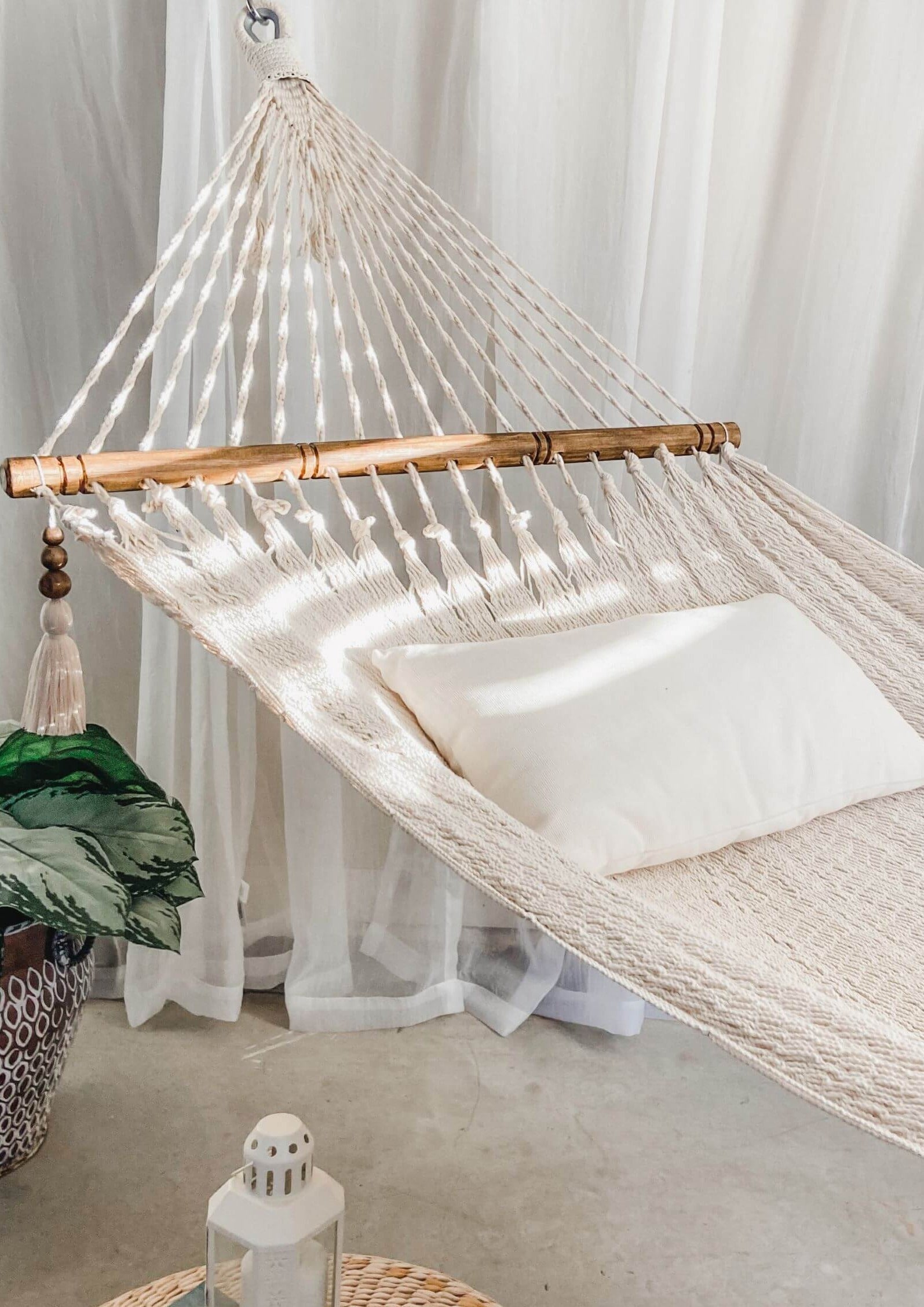 White hammock with wooden bars and a white pillow, set against a white curtain background.