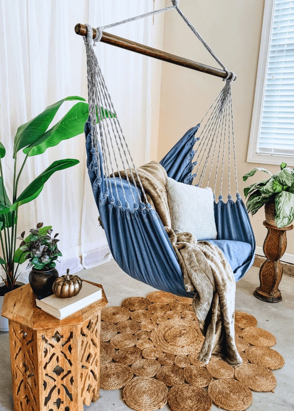 Blue hammock chair with pillows and blanket in a cozy room with plants and decor.
