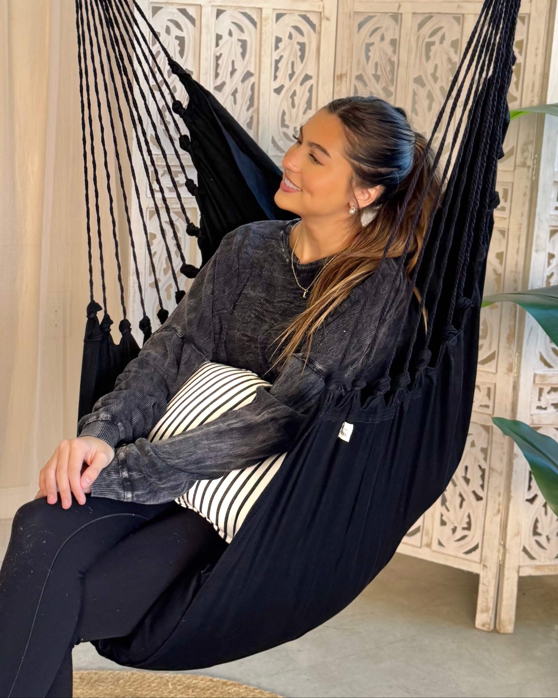 Woman sitting in a black hammock with a striped pillow, smiling.