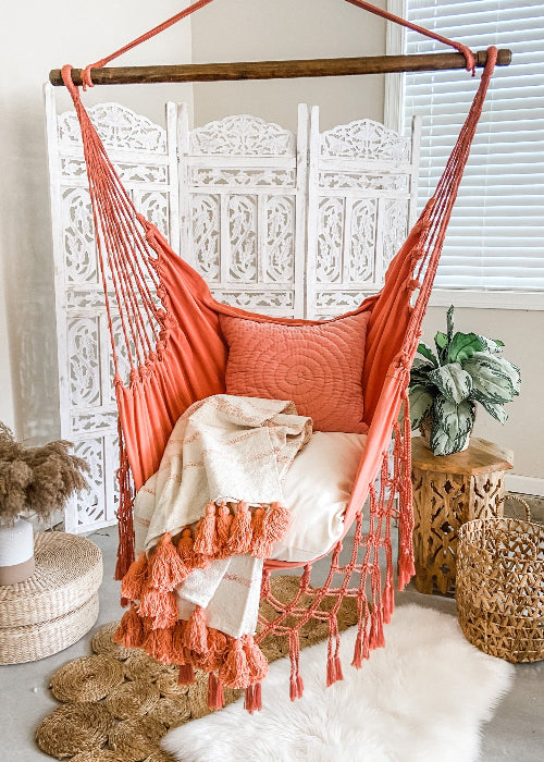Coral hammock chair with pillows and a blanket in a cozy room setting.