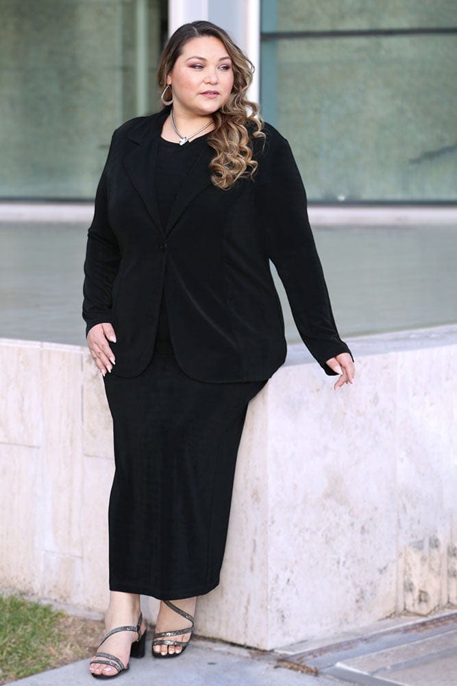 Woman wearing a black suit standing against a building.