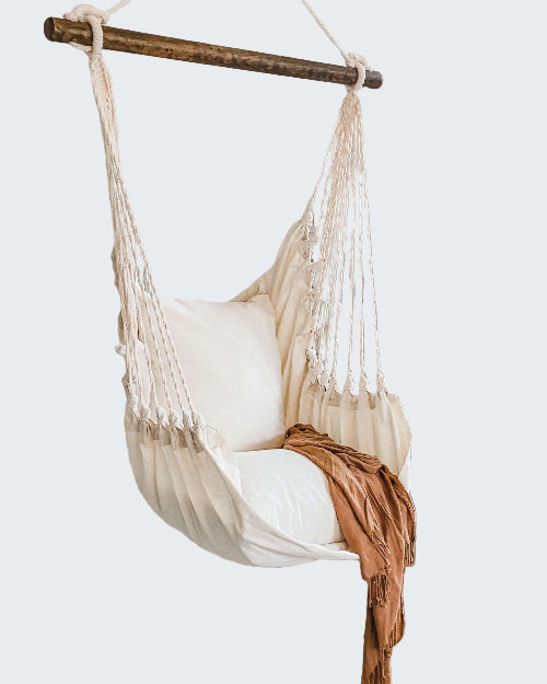 White hammock chair with a blanket in a room with a textured white wall and plant.