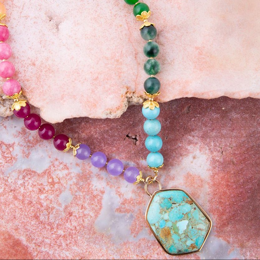 Beaded necklace with a turquoise pendant on a textured pink surface