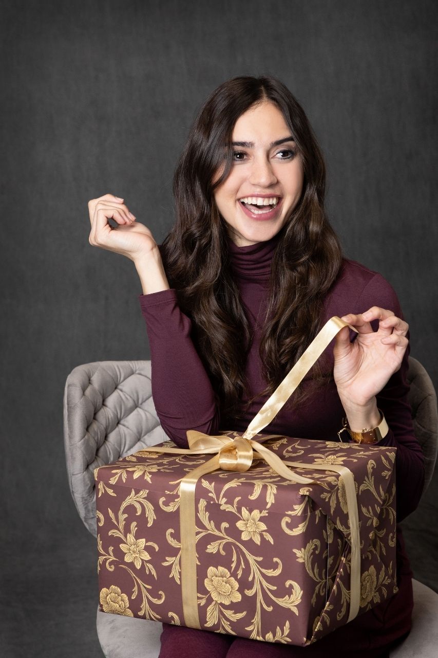 Woman opening a large gift box with a gold ribbon against a dark background