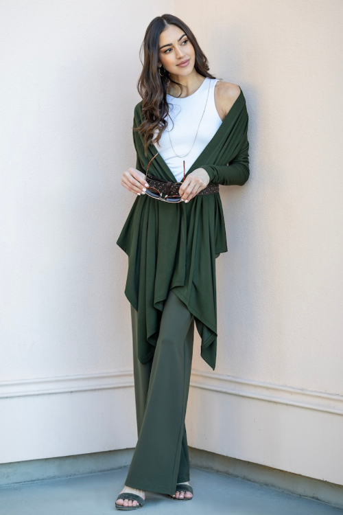 Woman wearing a green outfit with a white top against a light-colored wall.