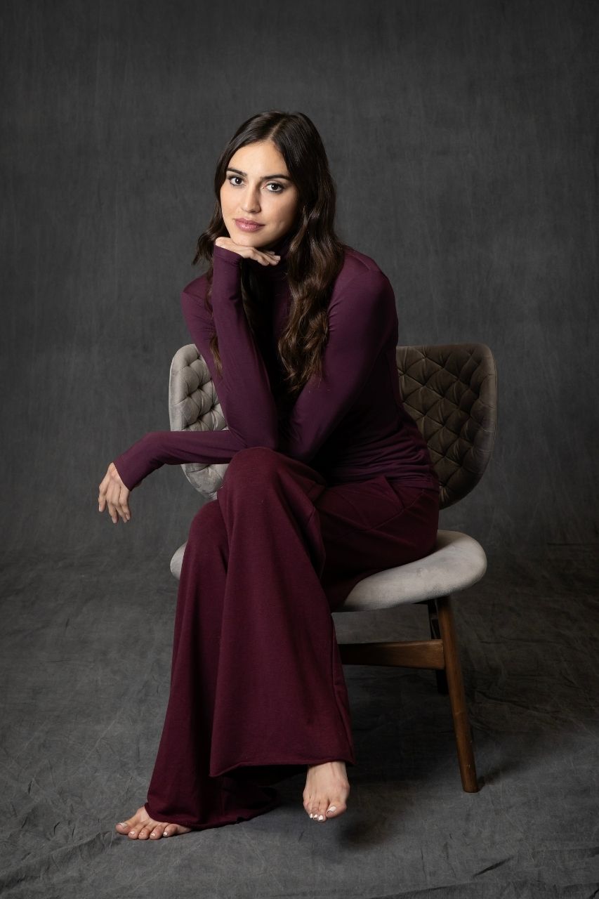 Woman in a long burgundy dress sitting on a chair against a dark background