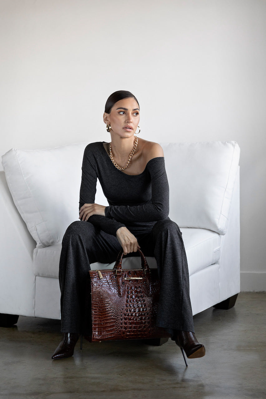 Woman in a black outfit holding a brown handbag on a white couch.