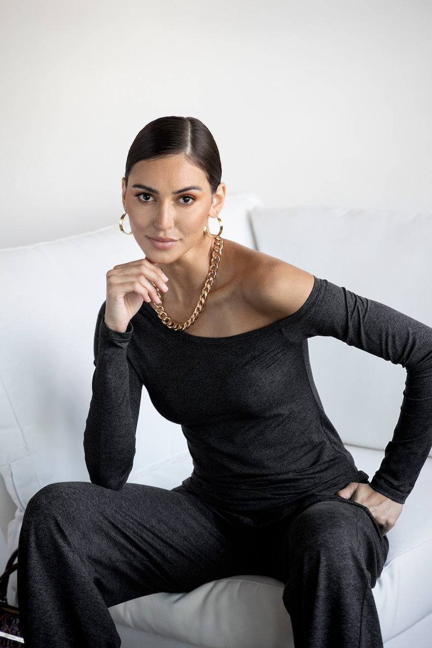 Woman in a black outfit sitting on a white couch with a plain background