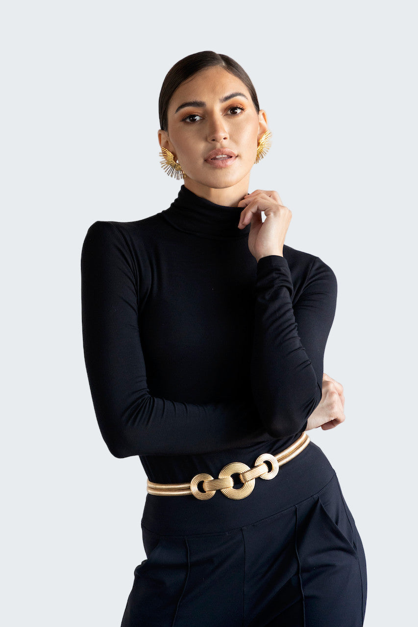 Woman wearing a black turtleneck and gold belt against a white background