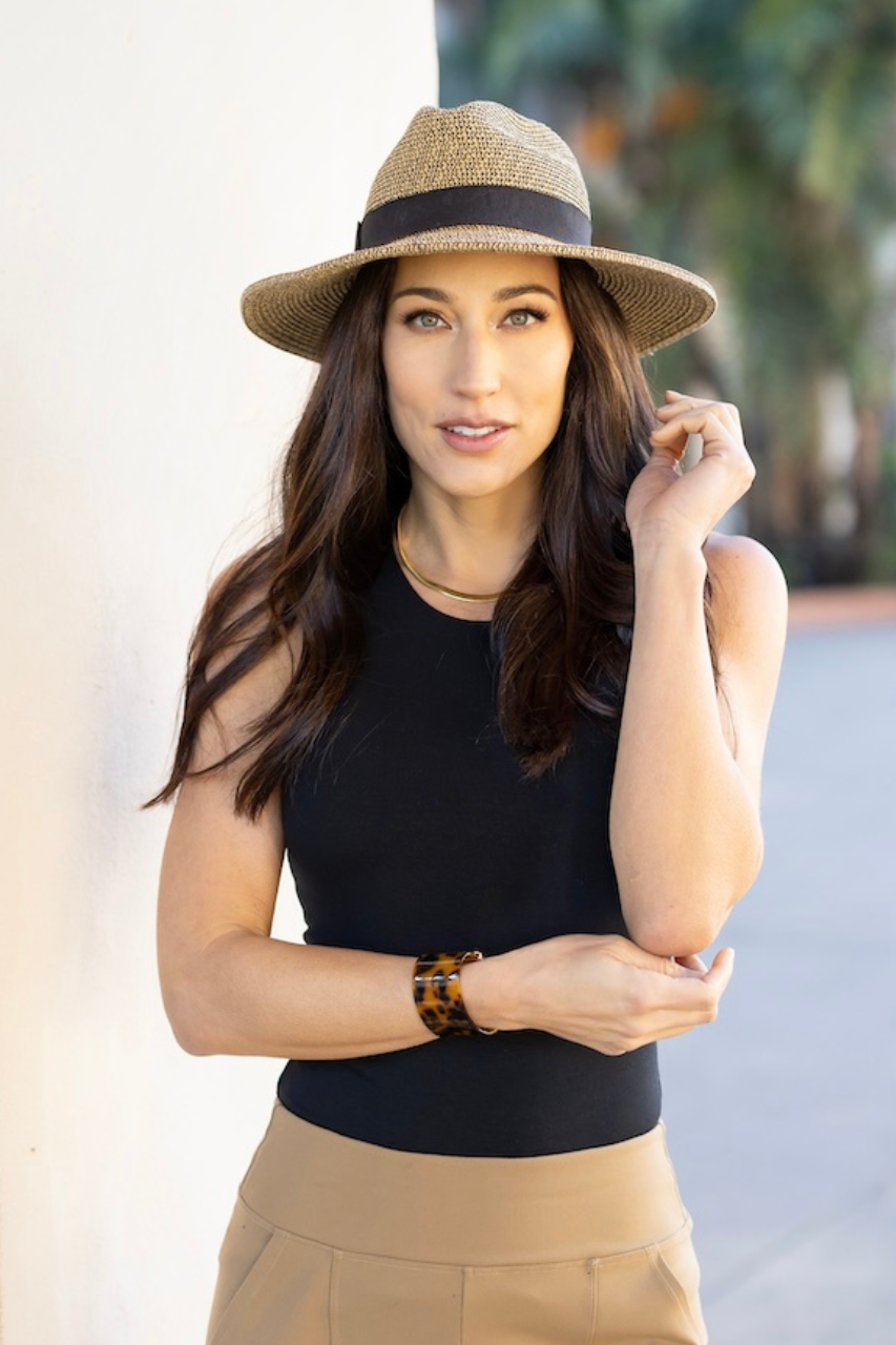 Woman wearing a black sleeveless top and beige hat with a blurred outdoor background