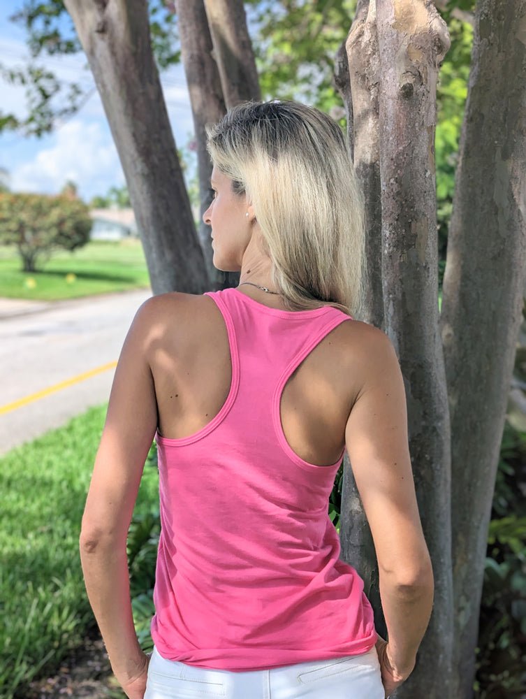 Woman in a pink tank top standing next to a tree outdoors