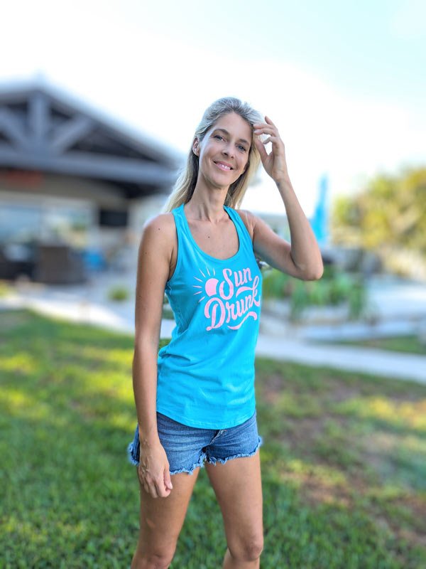 Woman wearing a blue tank top with 'Sun Dancer' text outdoors.