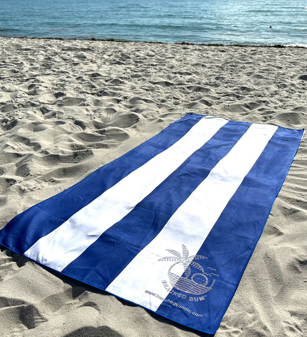 Blue and white striped towel on a sandy beach with ocean in the background