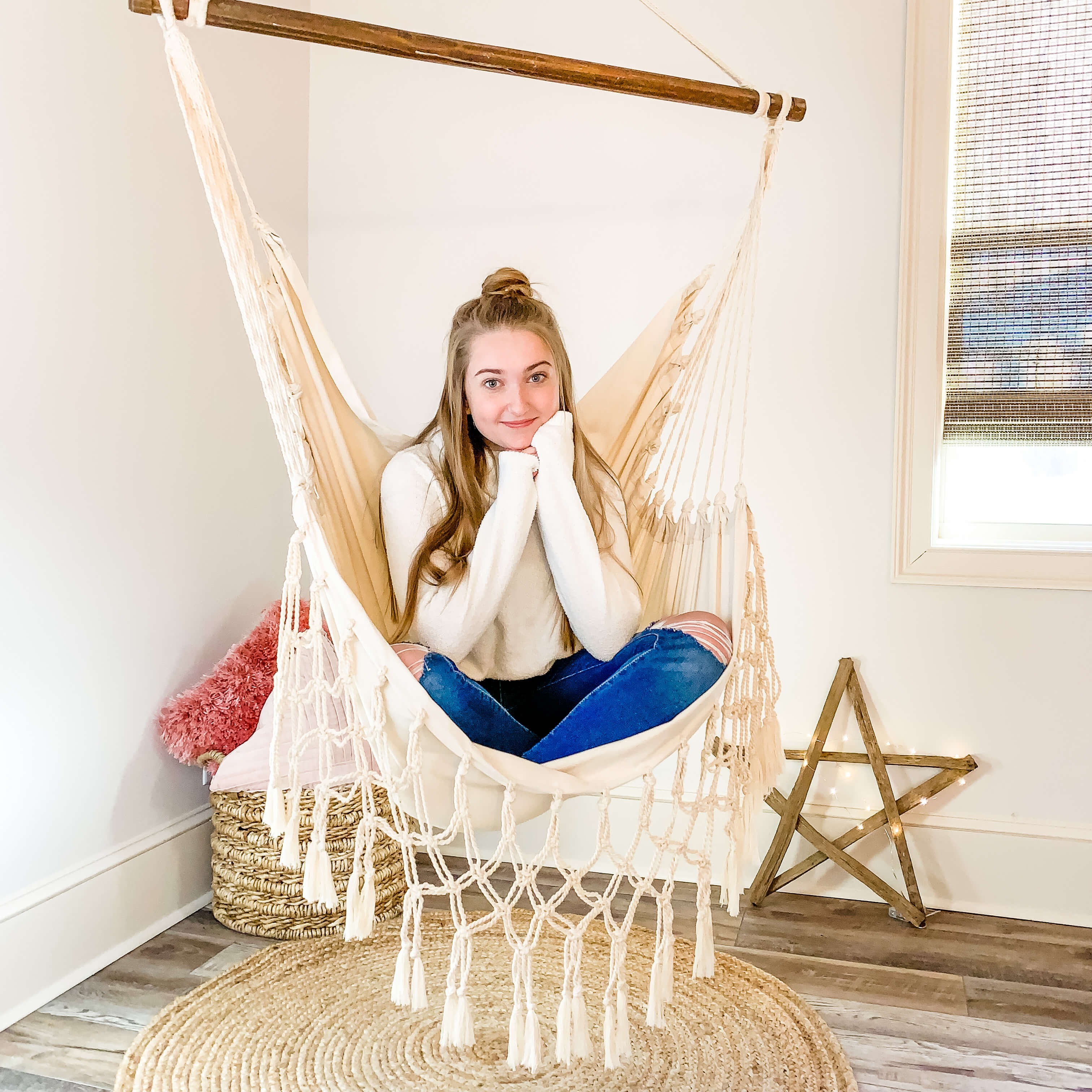 Woman sitting in a macrame hammock chair in a room with a star decoration on the wall.