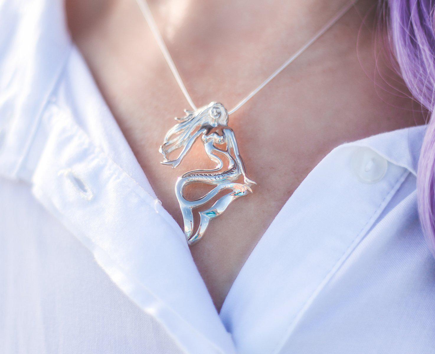 Silver necklace with a mermaid pendant worn by a person in a white shirt.