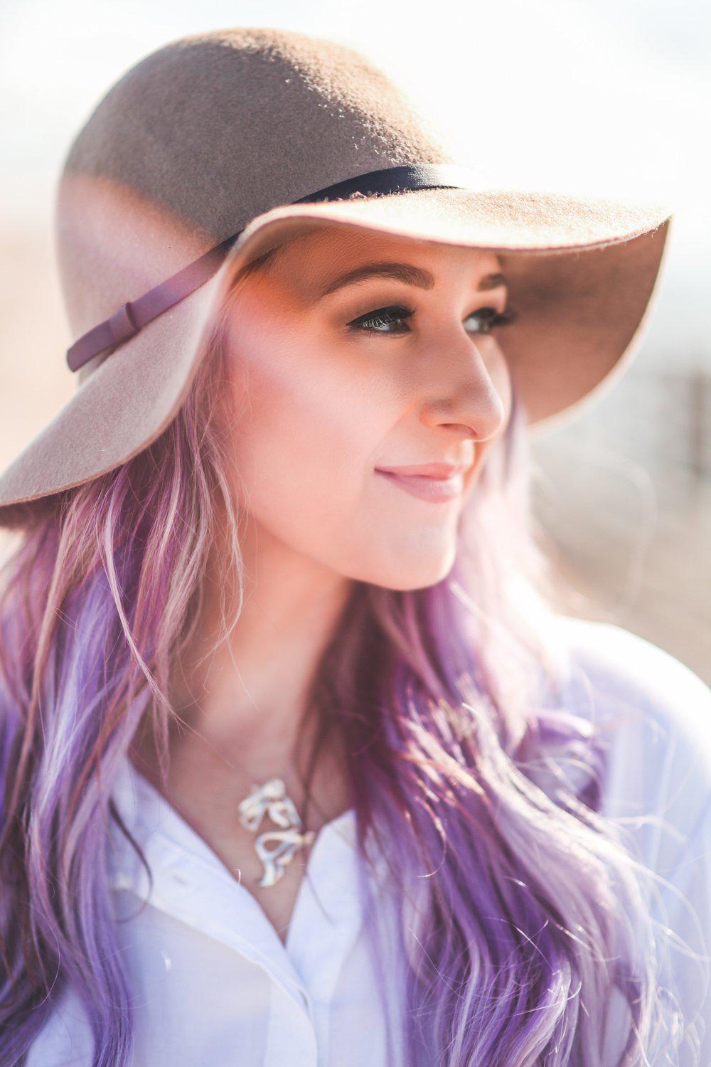 Woman with purple hair wearing a wide-brimmed hat in a sunlit outdoor setting