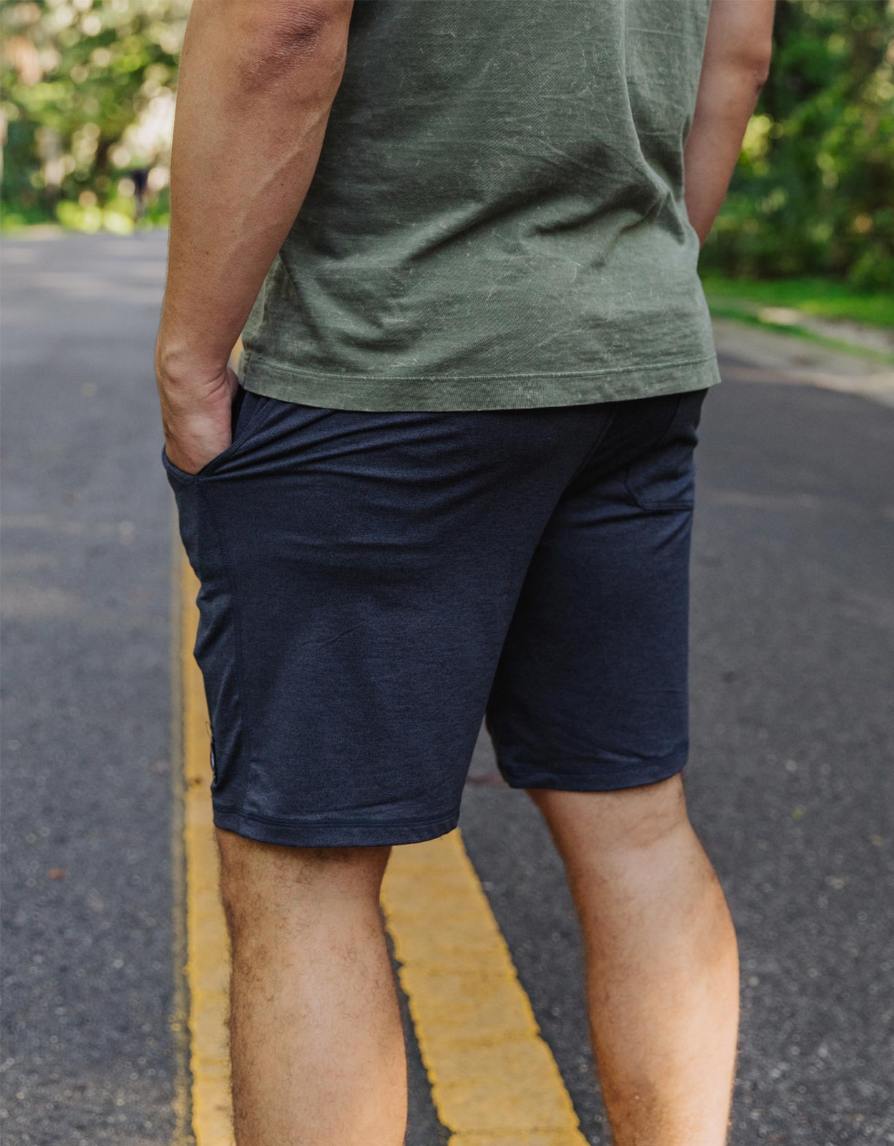 Person wearing a green t-shirt and navy shorts on a road with greenery in the background