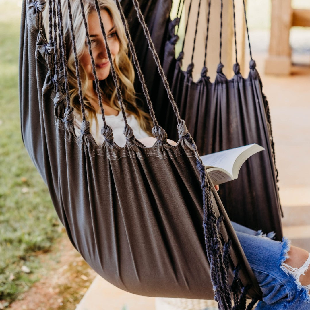 Woman sitting in a brown hammock reading a book outdoors