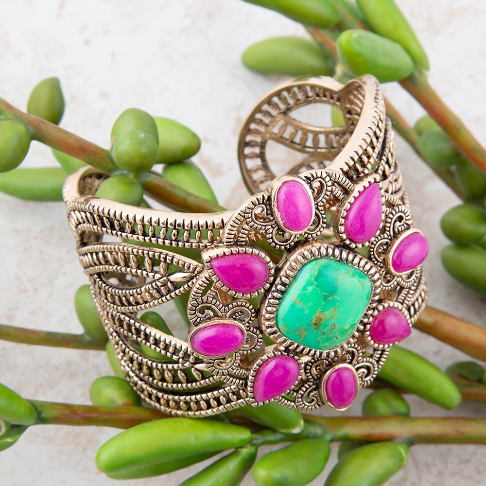 Decorative bracelet with pink and green stones on a green leaf background