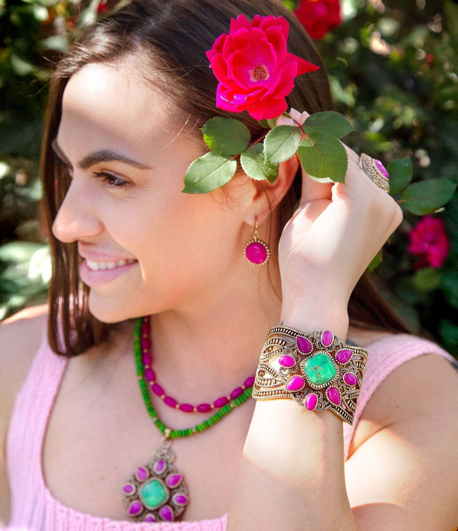 Woman wearing a pink dress with jewelry, including a bracelet and earrings, against a blurred natural background.