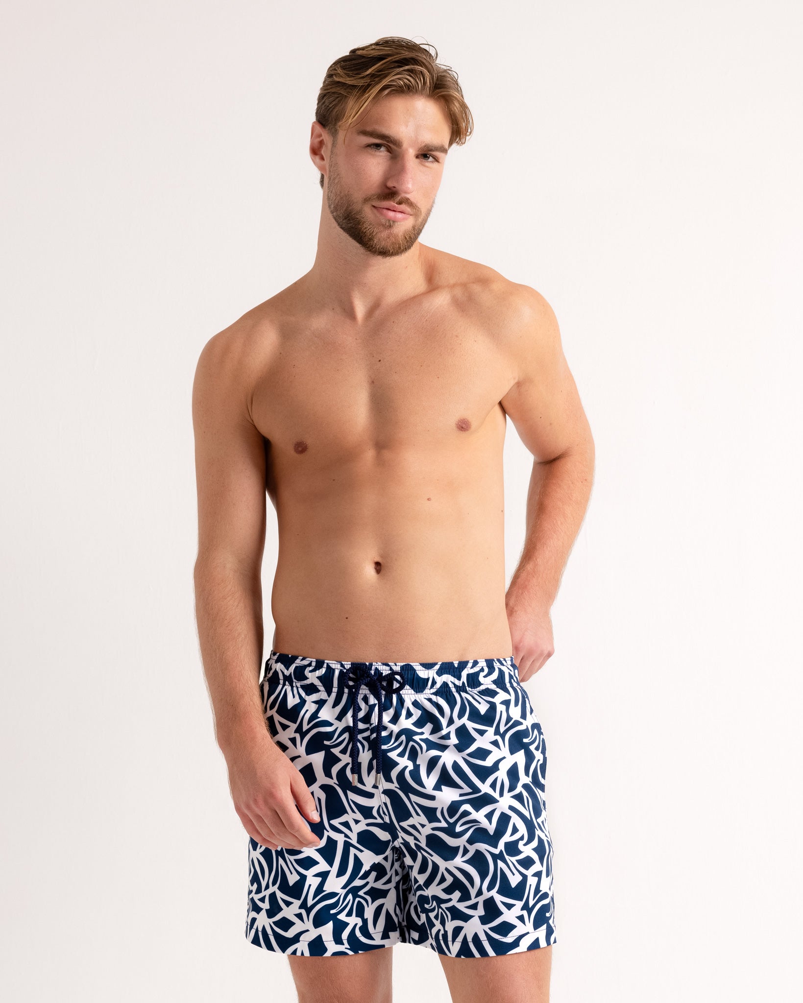 Man wearing navy blue swim shorts with white pattern on a light gray background